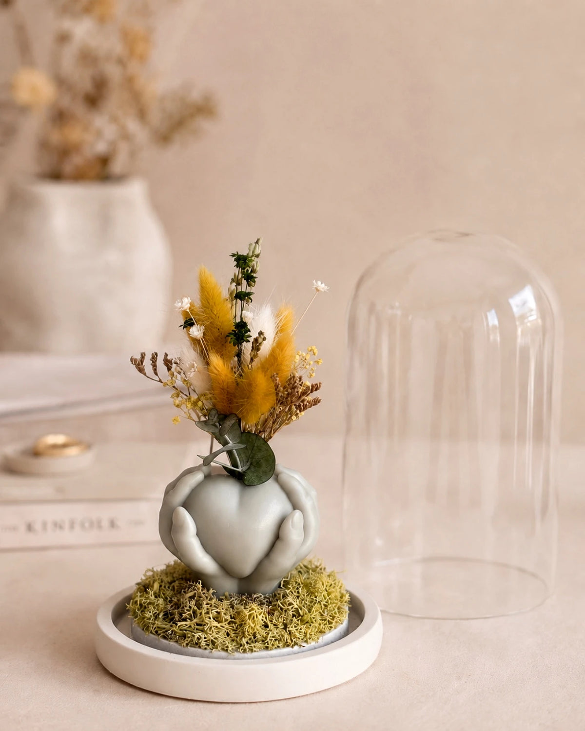 Carinho: composizione di fiori secchi in vaso di cera a forma di cuore sorretto da mani con campana di vetro e base di legno - Io Sono La Luce Roma | Colore verde salvia