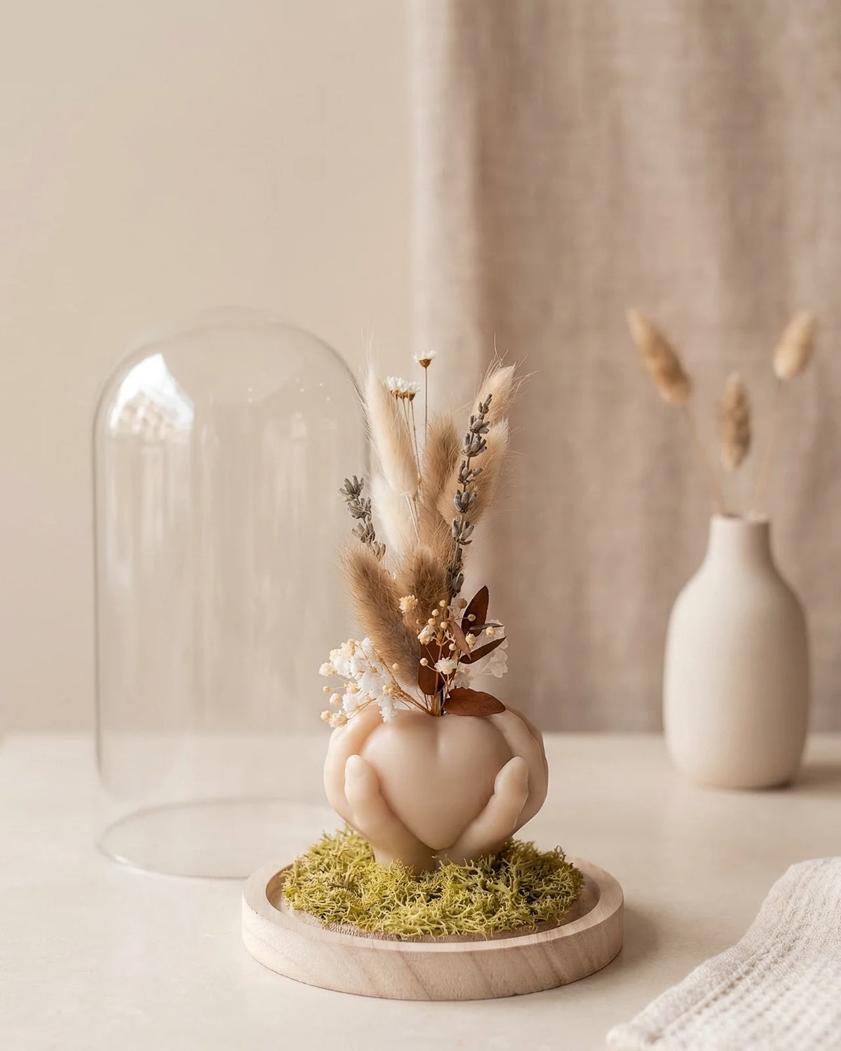 Composizione botanica artigianale con fiori secchi e stabilizzati sotto campana di vetro su base in legno naturale
