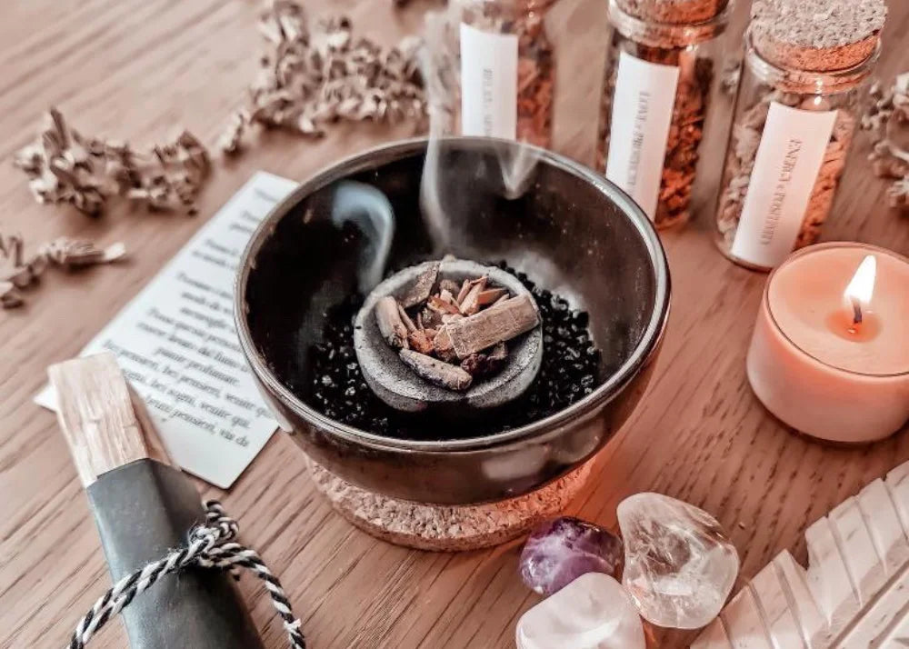 Fumo di Palo Santo che brucia in una ciotola, accompagnato da incensi naturali, cristalli e smudge per la purificazione degli ambienti e della mente.
