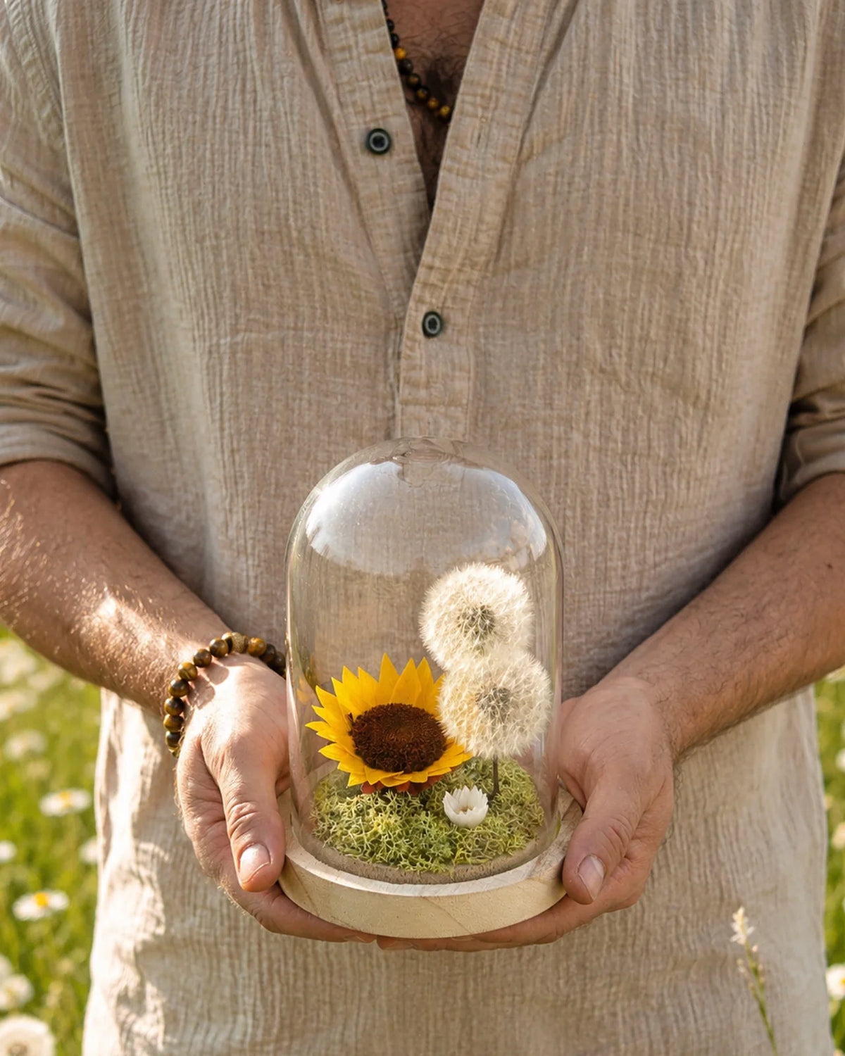 Mani che tengono la campana di vetro Alma Luciente con girasole e soffioni stabilizzati - terrarium botanico artigianale Io Sono La Luce