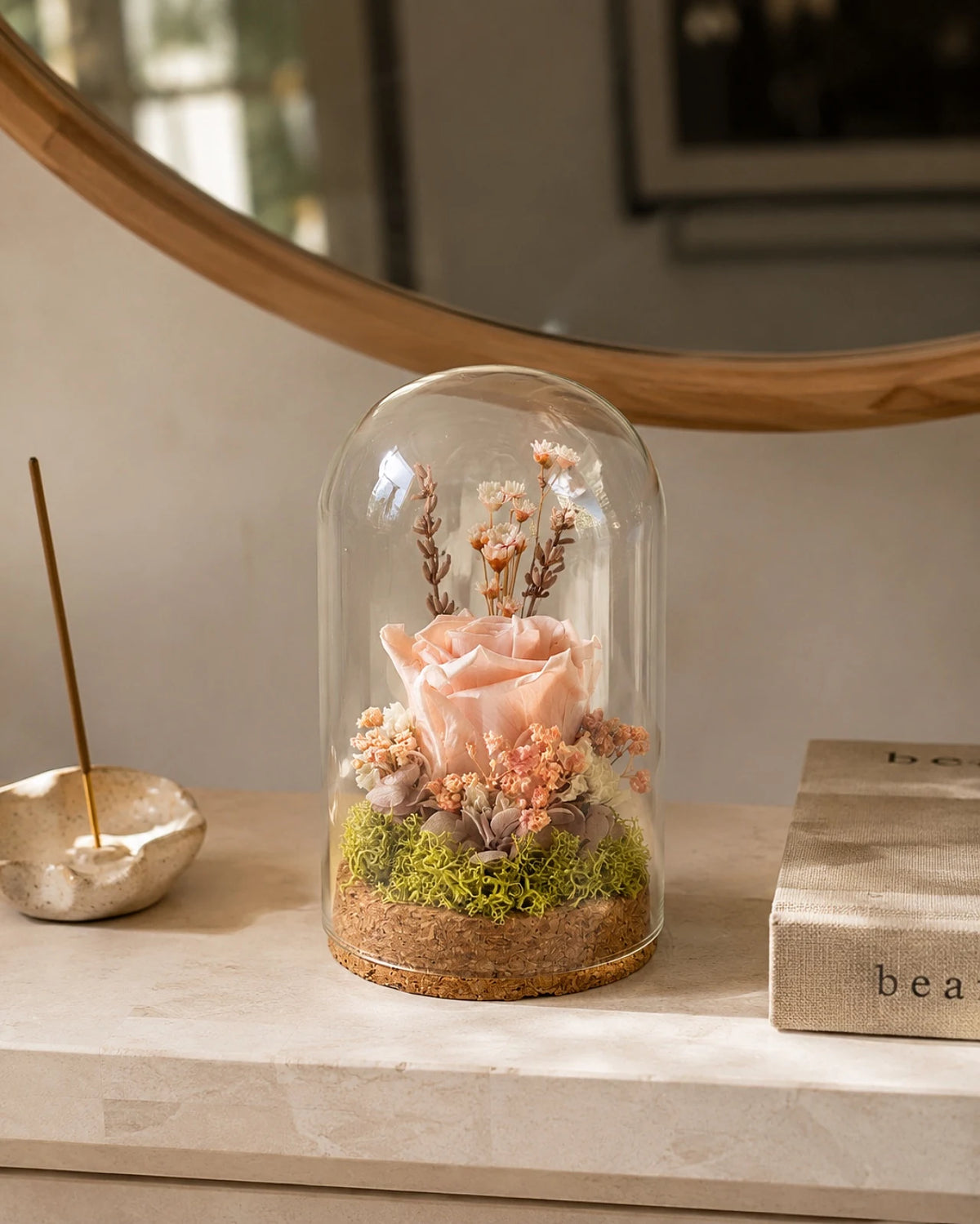 composizione di fiori stabilizzati e fiori secchi con rosa stabilizzata in campana di vetro e base di sughero su consolle 