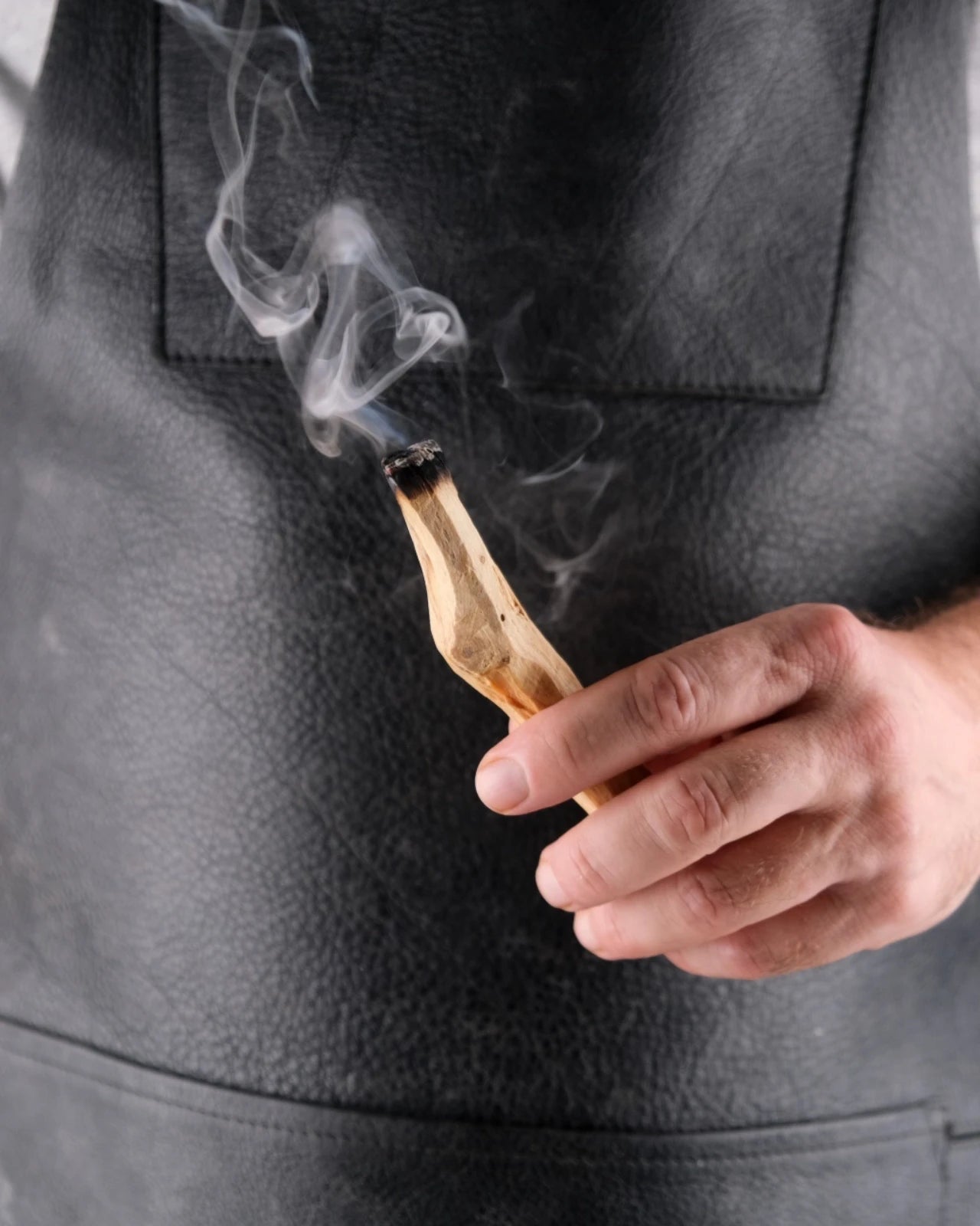 Mano che tiene un bastoncino di Palo Santo acceso con il fumo che sale, gesto di fumigazione